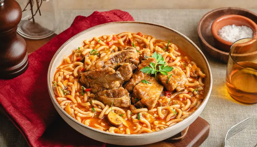 Un reconfortante plato de fideos a la cazuela con costilla, servido en un cuenco rústico, con un toque de perejil fresco.