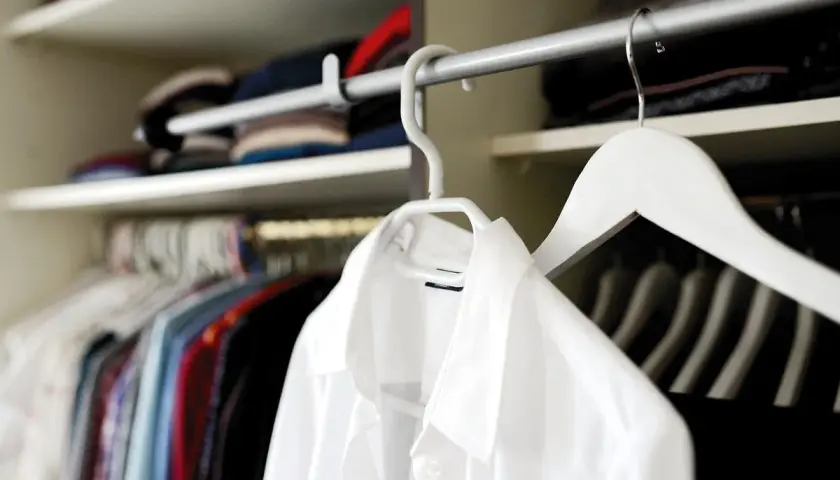 Chemises colorées et une chemise blanche en polyester, suspendues dans une penderie.