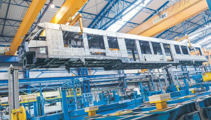 Szkielet wagonu kolejowego w hali produkcyjnej Alstom Chorzów, unoszony przez suwnicę.