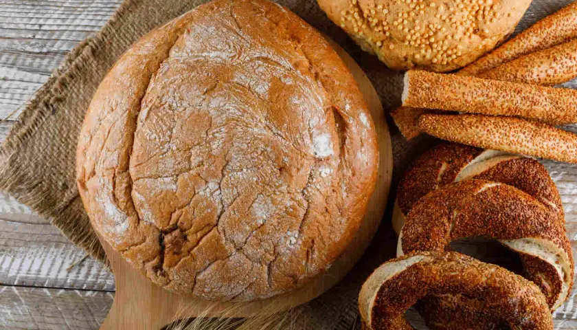 Różne rodzaje pieczywa: bochenek, paluszki sezamowe, obwarzanki i chleb z ziarnami.