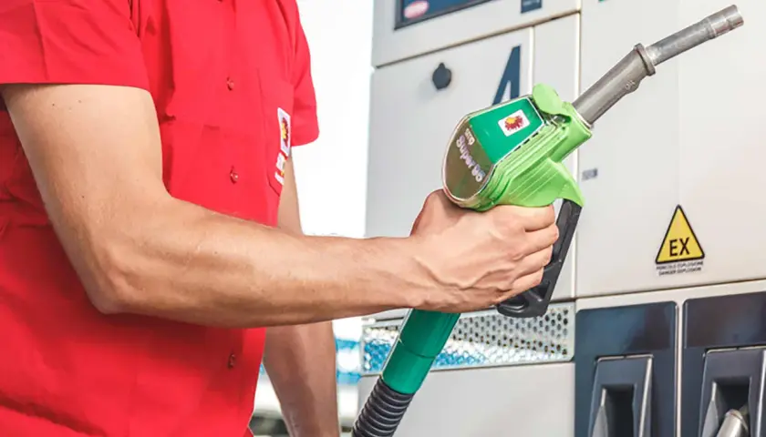 Un uomo in camicia rossa tiene una pompa di benzina verde con la scritta "Super 95".