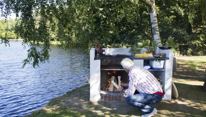 Man tänder en murad grill vid en sjö.