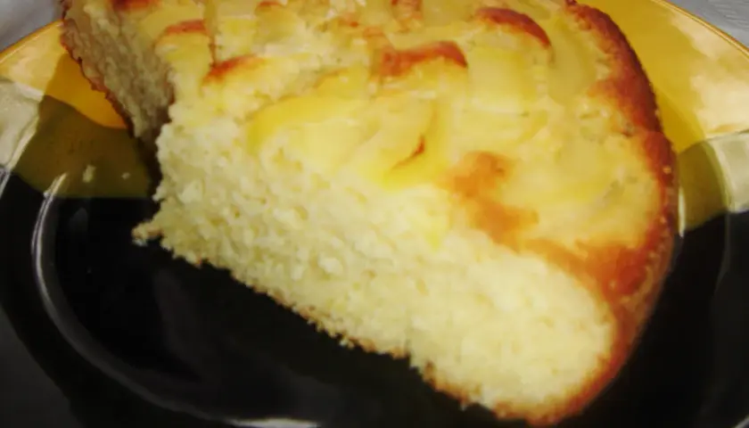 Proste ciasto z kawałkami jabłek, lekko zarumienione na brzegach, podane na czarno-żółtym talerzu.