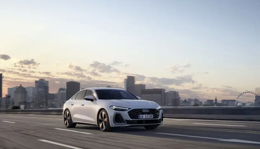 Białe audi hybryda jedzie po autostradzie z widokiem na miasto o zachodzie słońca.