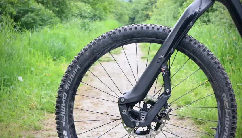 Close-up of a mountain bike's front wheel and fork on a dirt path, ready for adventure. This setup inspires trust and performance on any trail.