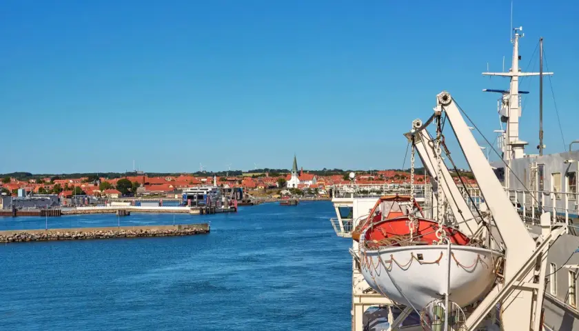 Widok na port z promem, łodzią ratunkową i miastem w tle.