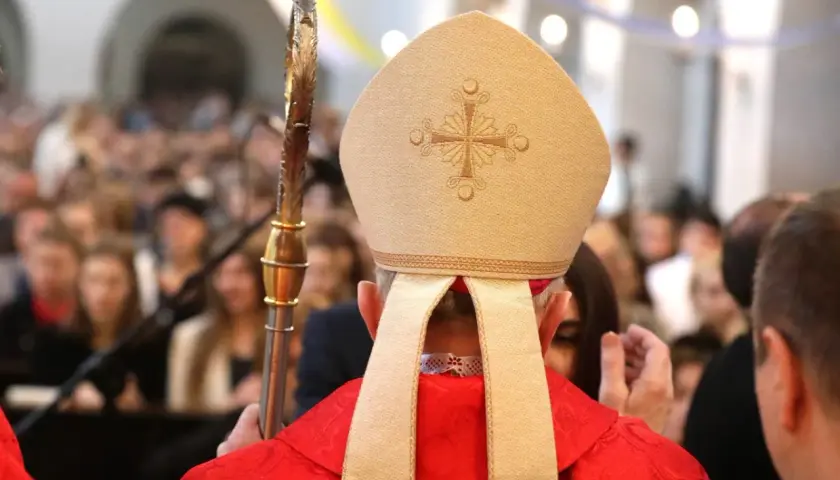 Biskup w mitrze i czerwonej szacie, trzymający pastorał, udziela sakramentu. Zastanawiasz się, ile trwa bierzmowanie?
