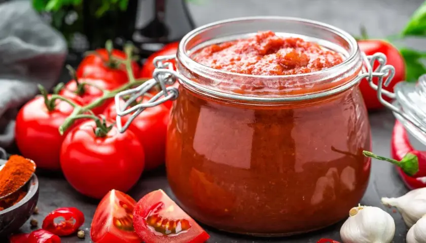 Słoik domowego sosu z przecieru pomidorowego, obok świeże pomidory, czosnek i papryczki chili. Idealny przepis, jak zrobić sos z przecieru pomidorowego.