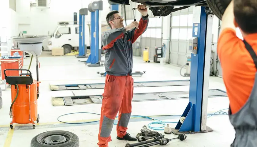 Mecánicos trabajando en el mantenimiento de coches en un taller. Uno usa una llave inglesa en el coche elevado, otro se prepara.