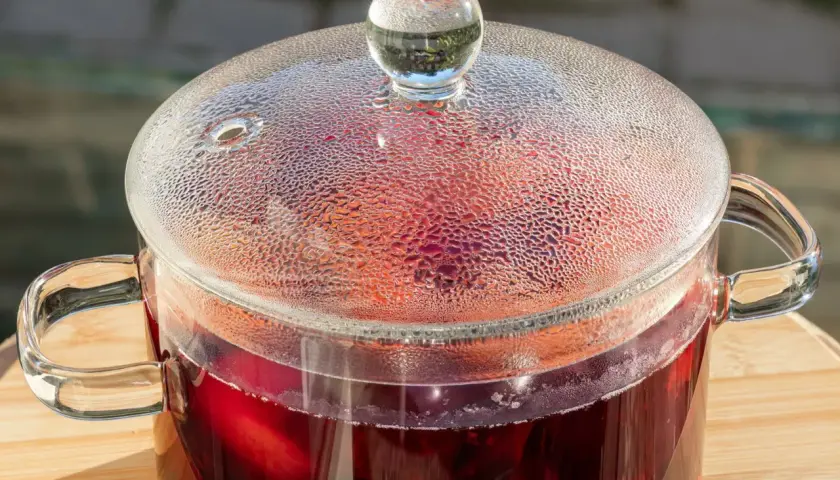 Szklany garnek z parującym, rubinowym kompotem ze śliwek. Krople pary na pokrywce tworzą wzór.