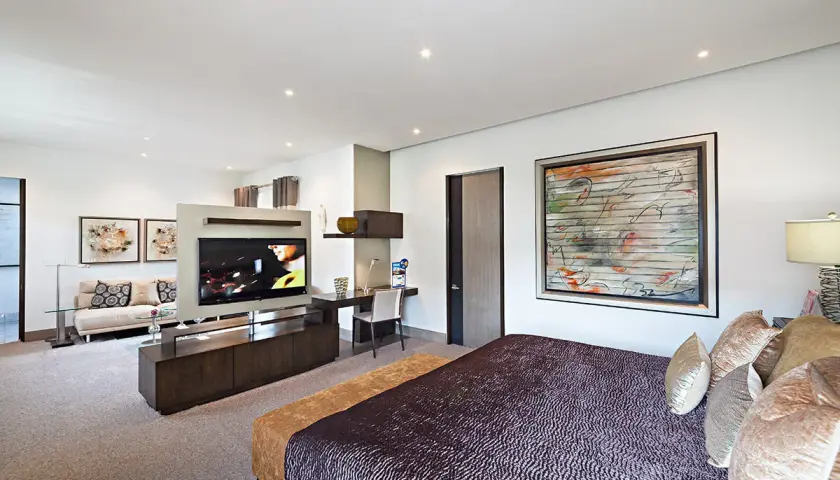 Modernes Schlafzimmer mit einem großen Fernseher im Wohnbereich, der durch eine Trennwand vom Bett abgetrennt ist.