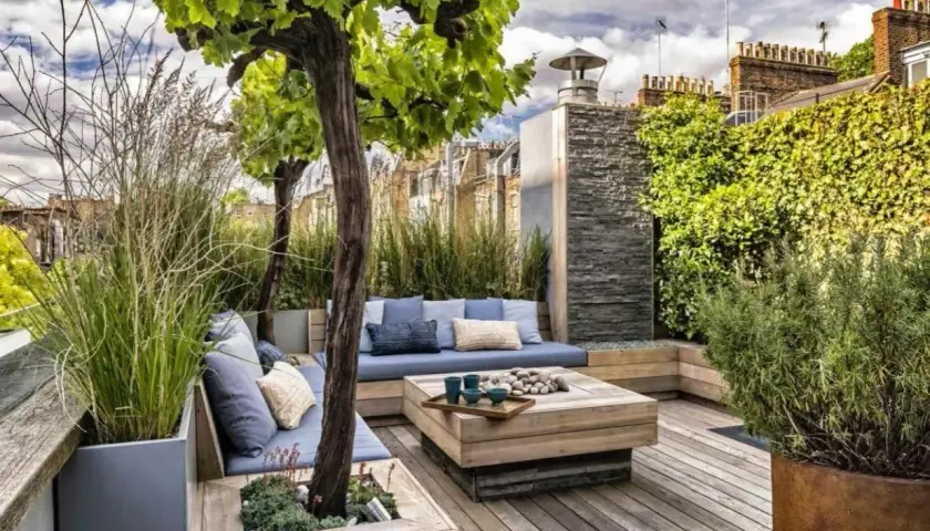 Aménagement autour d'une terrasse avec banquette bleue, table basse en bois et végétation luxuriante. Un espace détente chic et verdoyant.