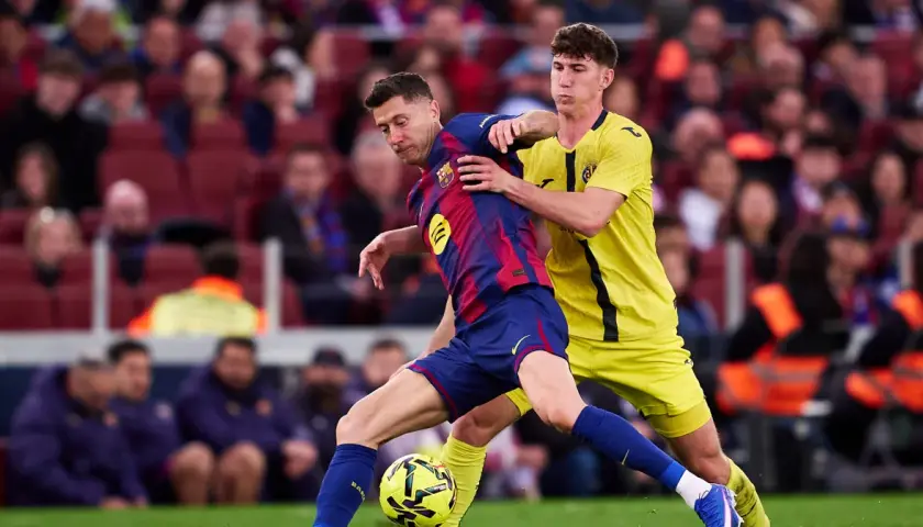 Piłkarz Barcelony Robert Lewandowski w akcji, walczy o piłkę z obrońcą. Kibice na trybunach obserwują mecz, martwiąc się o lewandowski kontuzja.