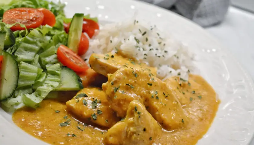 En krämig kyckling korma med ris och en fräsch sallad på tomat och gurka.