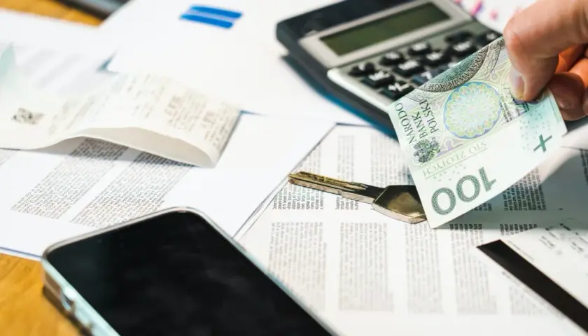 Dłoń trzyma banknot 100 zł obok klucza i dokumentów. Rozważasz grupy podatkowe darowizna?