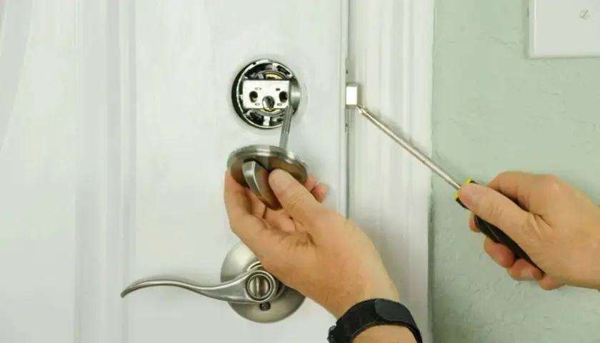 Main tenant démonte une poignée de porte pour savoir comment ouvrir une porte de chambre bloquée.