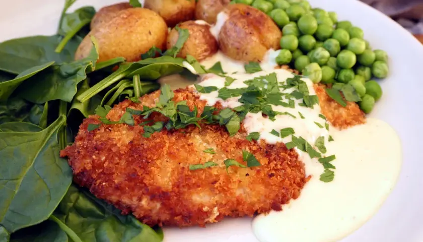 Krispig schnitzel med krämig sås till, serverad med småpotatis, gröna ärtor och färsk spenat.
