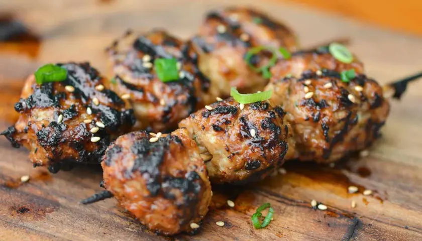 Skewered, grilled Japanese meatballs glazed with a savory sauce, sprinkled with sesame seeds and green onions.