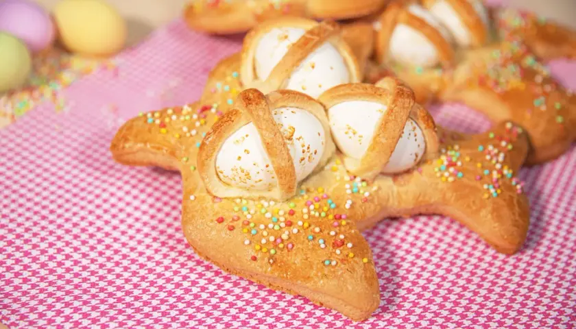 Scarcelle pugliesi ricetta originale: dolci a forma di colomba con uova sode, decorati con zuccherini colorati su tovaglia a quadretti rosa.