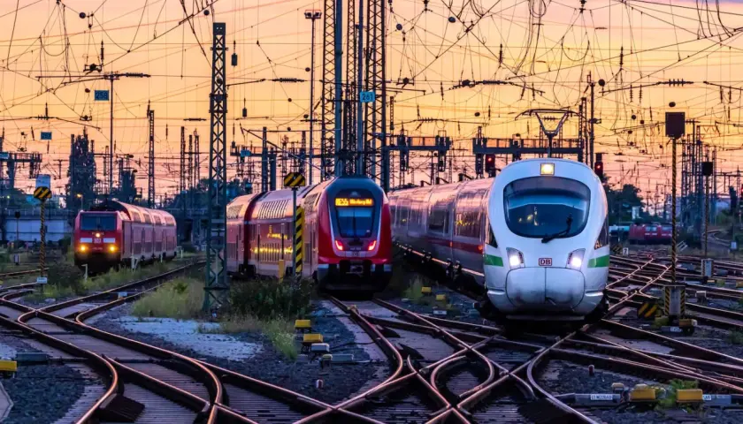 Mehrere Züge auf Bahngleisen bei Sonnenuntergang. Das Deutschlandticket gilt einen Monat lang.