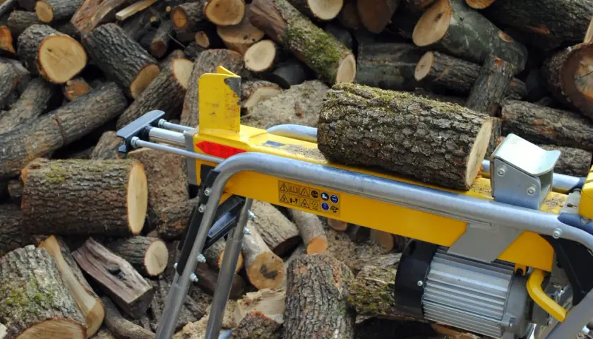 Ein gelber Holzspalter 1m liegt bereit, um den Stapel geschnittener Baumstämme zu bearbeiten.