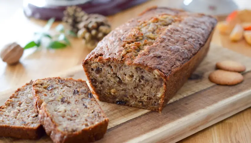 Un délicieux cake banane, coupé en tranches, sur une planche en bois. Des noix et des biscuits complètent cette gourmandise.