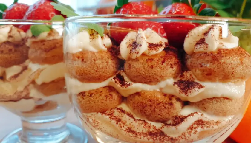 Pyszne tiramisu w pucharkach, przełożone kremem i biszkoptami, ozdobione truskawkami i kakao.