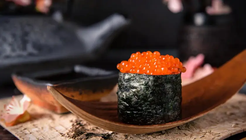 Wykwintny gunkan sushi z łososiem ikra, owinięty w ciemne nori, prezentowany na drewnianej łódce.