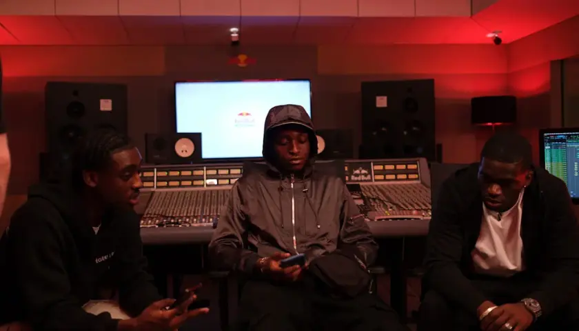 Trois jeunes hommes dans un studio d'enregistrement, discutant peut-être d'un cover rap gratuit.
