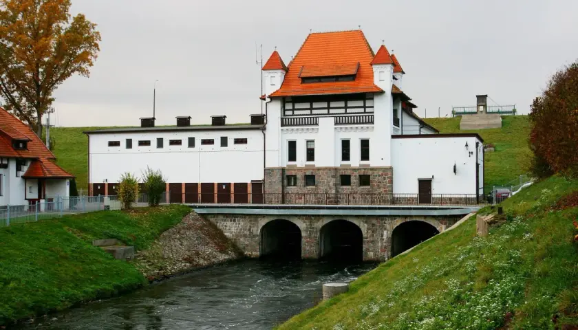 Elektrownia wodna Straszyn z charakterystycznym czerwonym dachem i kamienną podstawą, nad rwącą rzeką.