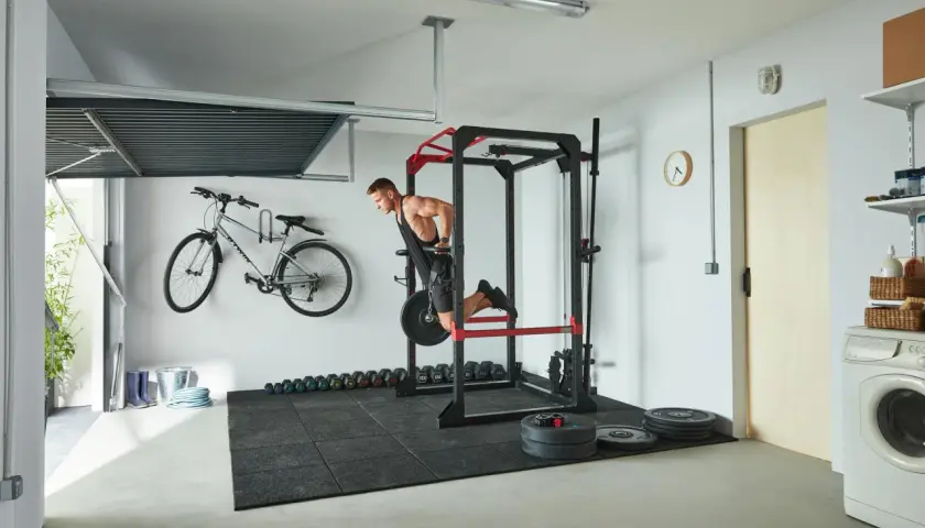 Mężczyzna wykonuje ćwiczenia na środek klatki piersiowej na drążku. W tle rower, hantle i sprzęt do treningu siłowego.