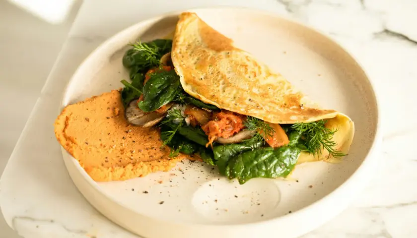 Omlet z air fryera z farszem ze szpinaku, grzybów i kimchi, podany z pomarańczowym hummusem.