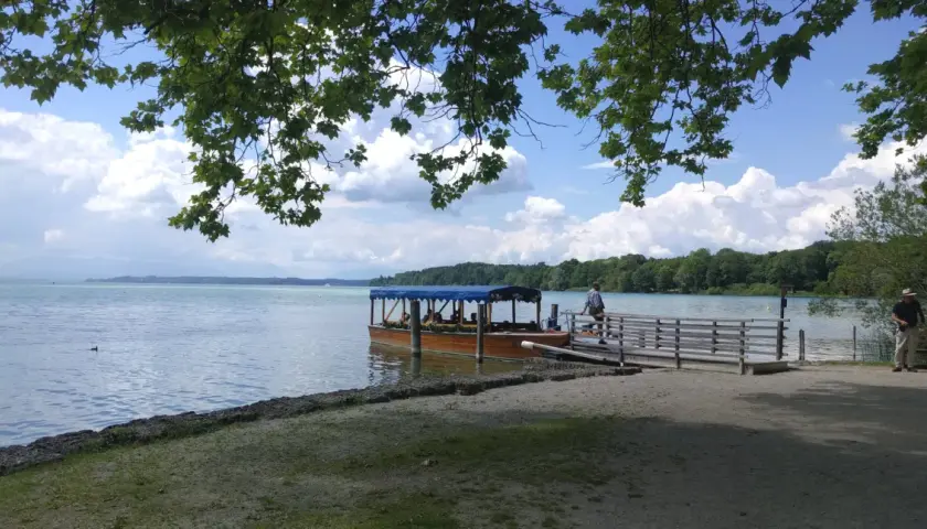 Ein Ausflugsboot wartet am Steg am Starnberger See. Zwei Männer sitzen auf einer Bank im Schatten.