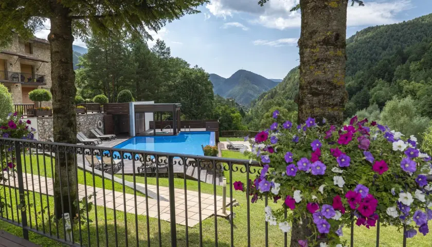 Un hotel de montaña con piscina azul, rodeado de vegetación. La coma i la pedra, un lugar de ensueño.