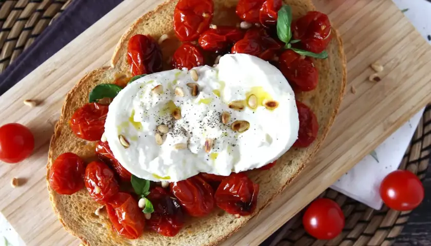 Pyszna bruschetta z burratą, pieczonymi pomidorkami koktajlowymi i orzeszkami pinii. Idealna na lekki posiłek.