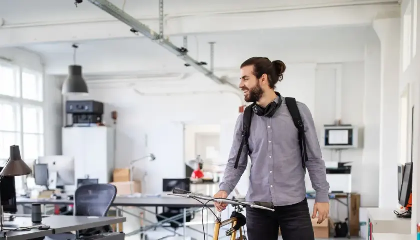 Junger Mann mit Fahrrad und Rucksack im Büro, bereit für sein online studium in Berlin.