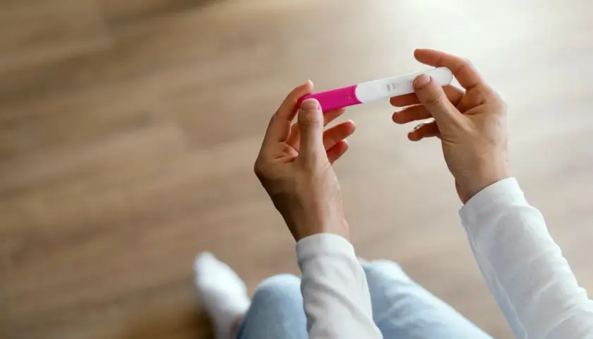 Dłonie trzymające test ciążowy, który może wskazać pierwsze objawy ciąży.