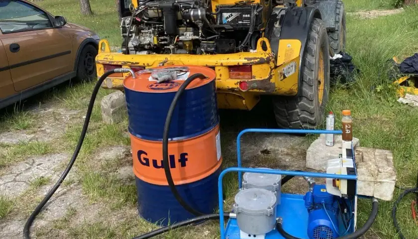 Jak sprawdzić poziom oleju hydraulicznego w koparce? Widać beczkę Gulf, pompę i wąż prowadzący do maszyny.