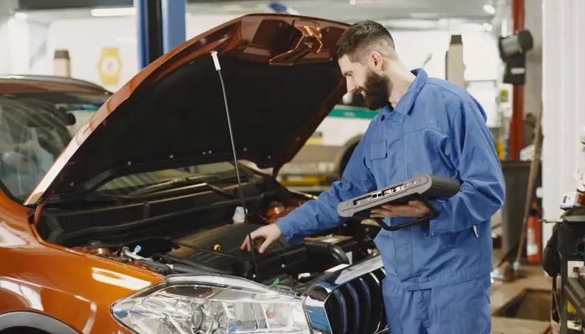Mechanik z komputerem diagnostycznym sprawdza silnik. Zastanawiasz się, jak długo trwa wymiana oleju? To zależy od modelu auta i doświadczenia mechanika.