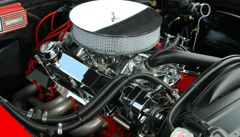 Błyszczący silnik V8 z chromowanymi elementami i czerwonymi przewodami zapłonowymi. Ten potężny motor, gotowy do pokonania wielu kw a km, to serce klasycznego muscle cara.