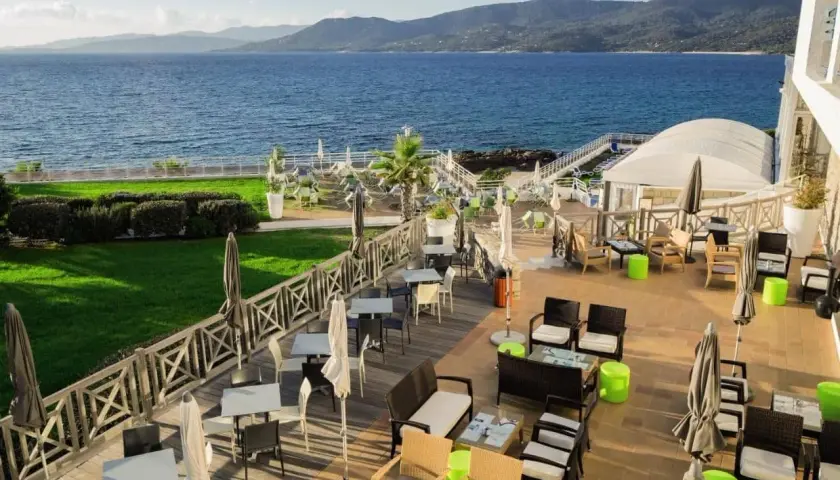 Terrasse d'un hôtel avec vue sur la mer, mobilier extérieur et verdure.