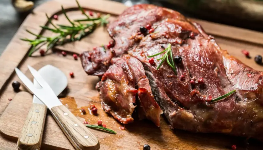 Soczysta dziczyzna, pieczona z rozmarynem i pieprzem, czeka na desce do krojenia. Obok leżą sztućce do mięsa.