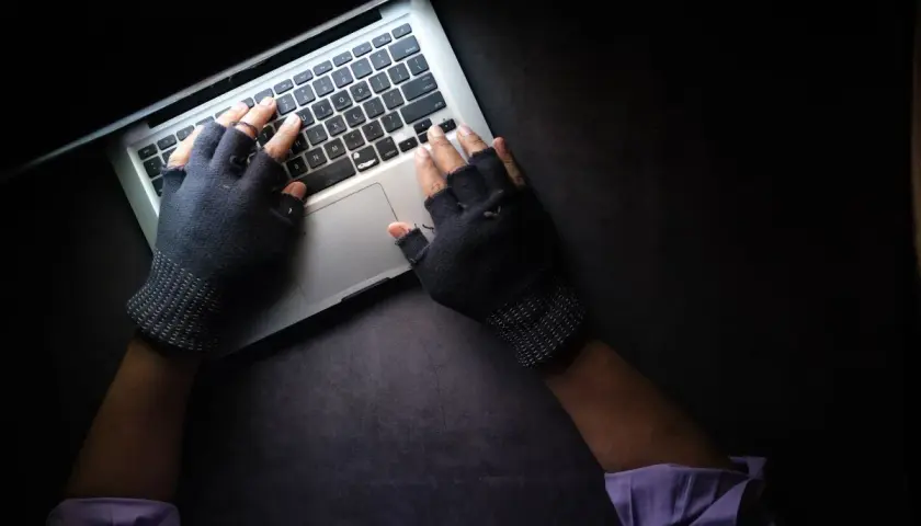 Ręce w rękawiczkach bez palców piszą na laptopie. To może być początek fascynujących studiów kryminalistycznych.