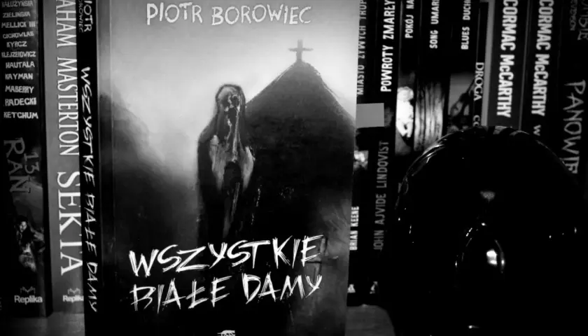 Okładka książki "Wszystkie białe damy" Piotra Borowca. Na okładce widnieje przerażająca postać i krzyż na kopcu.