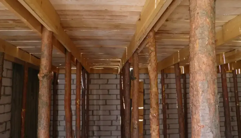 Szalowanie stropu z drewnianych belek i pni drzew, podtrzymujące konstrukcję nad ścianami z bloczków.