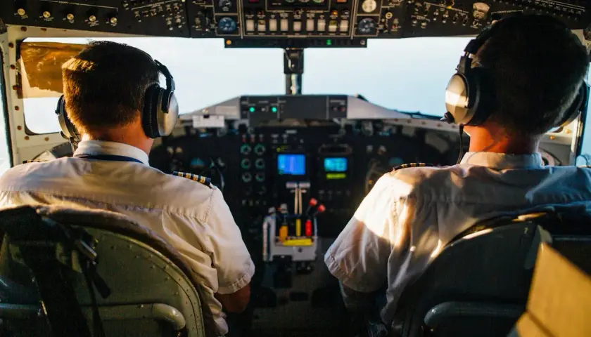 Dwóch pilotów samolotu w słuchawkach na tle kokpitu.