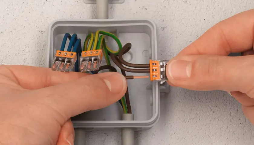 Mains électriques connectées dans une boîte encastrée. Le diamètre de la boîte encastrement permet d'accueillir les fils et les connecteurs.