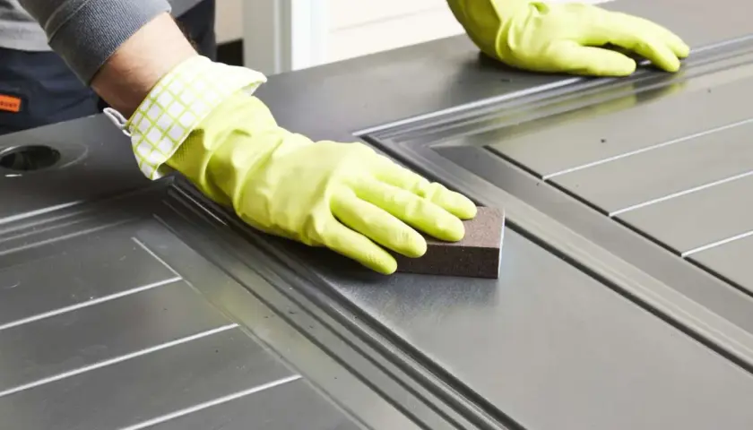 Manos enguantadas lijando una puerta para pintar aluminio.