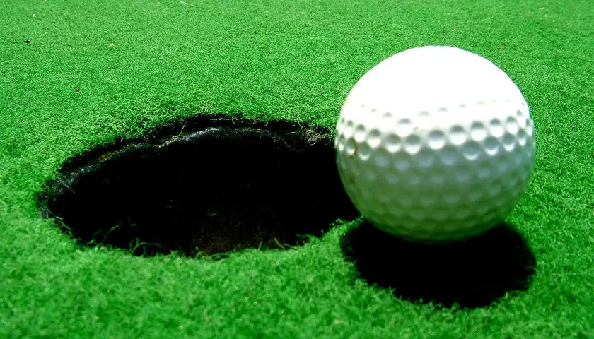 Vacker golfbana i Sverige med gröna fairways, bunkrar och vattenhinder. En flagga markerar ett golfhål med standard diameter.