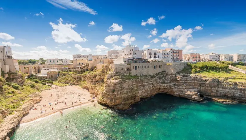 Vue panoramique de la plage de Polignano a Mare, avec ses falaises rocheuses, ses eaux turquoise et ses maisons blanches perchées.